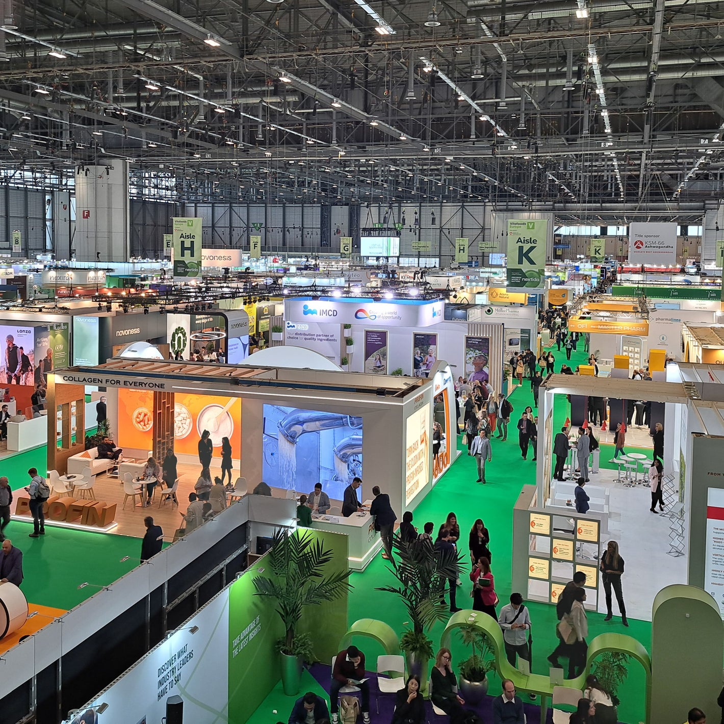 <Looking down at a large international supplier exhibition in a large hall with bright green walkways between stands. Credit> GMP-SOP-Download.com @ Vitafoods