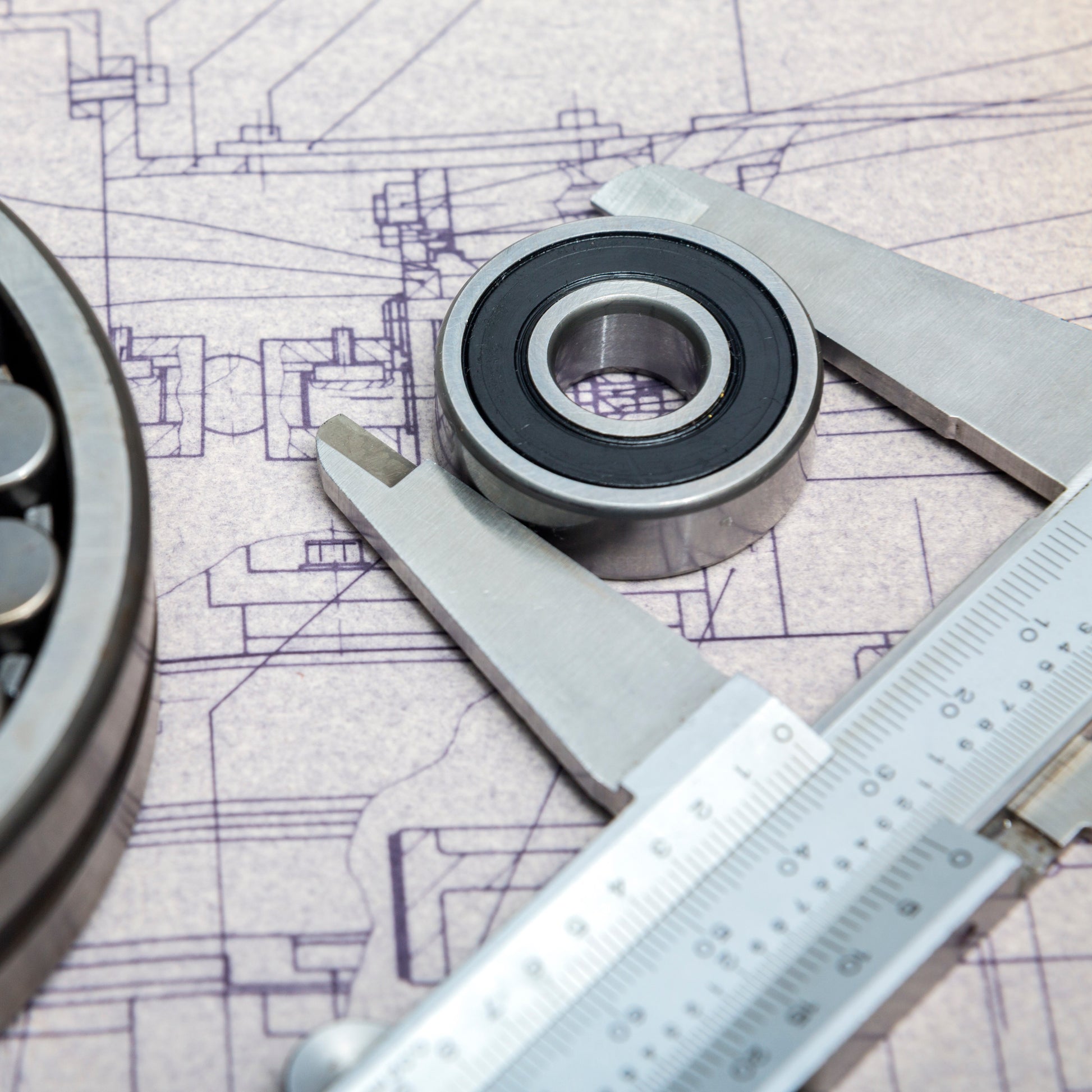 <Pair of stainless steel calipers measuring the diameter of a metal washer lying on a technical drawing of a production line from which the parts are taken. Credit> AdobeStock_132336449