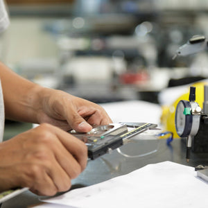 <Man calibrating a pressure gauge on a filling machine with blurred production background using some digital calipers and tubing. Credit> AdobeStock_136338979