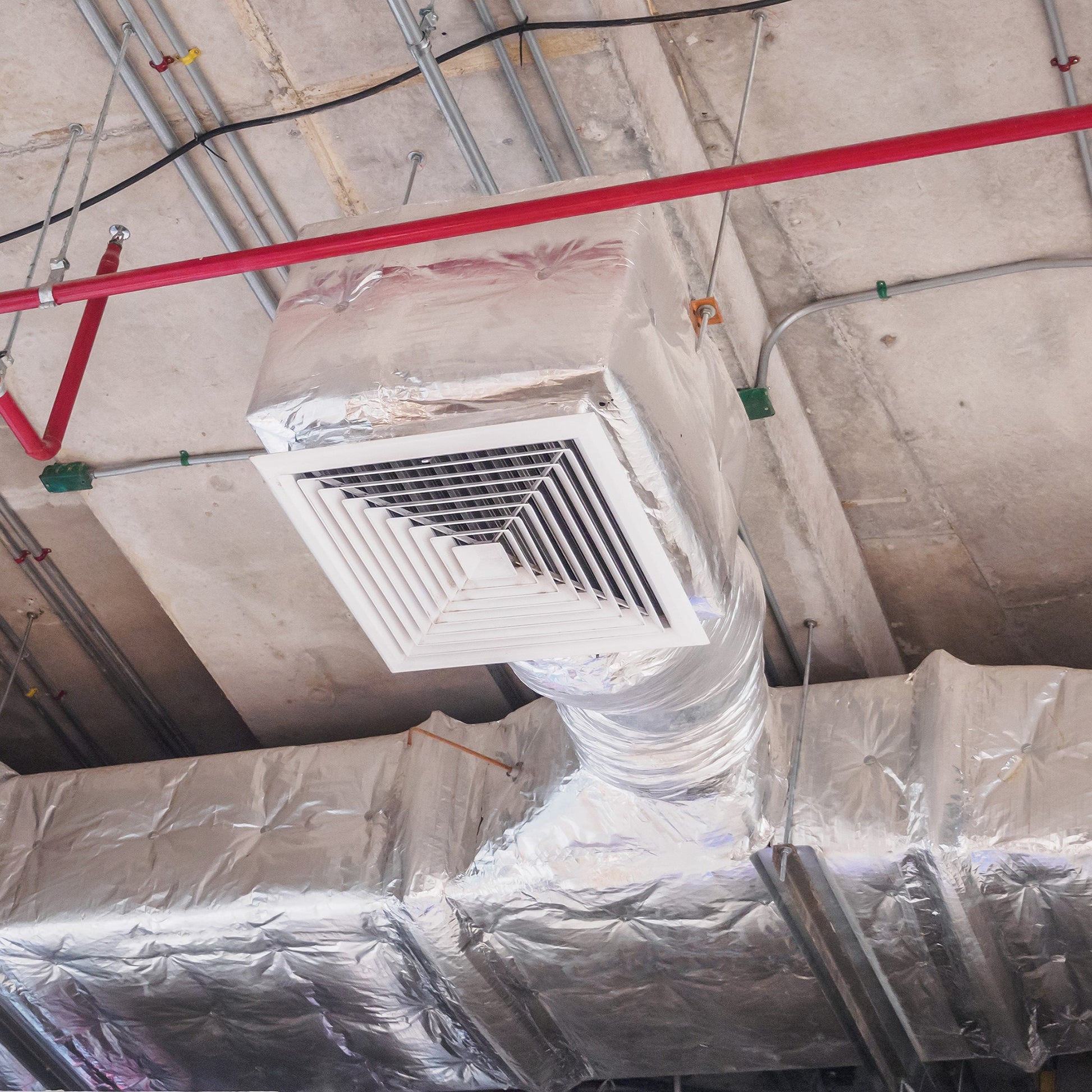 <Fire spray and air handling system with white square grid outlet and ducts covered in silver lagging on the concrete ceiling of a dietary supplement facility to provide fire protection, clean air and ventilation. Credit> AdobeStock_166402650