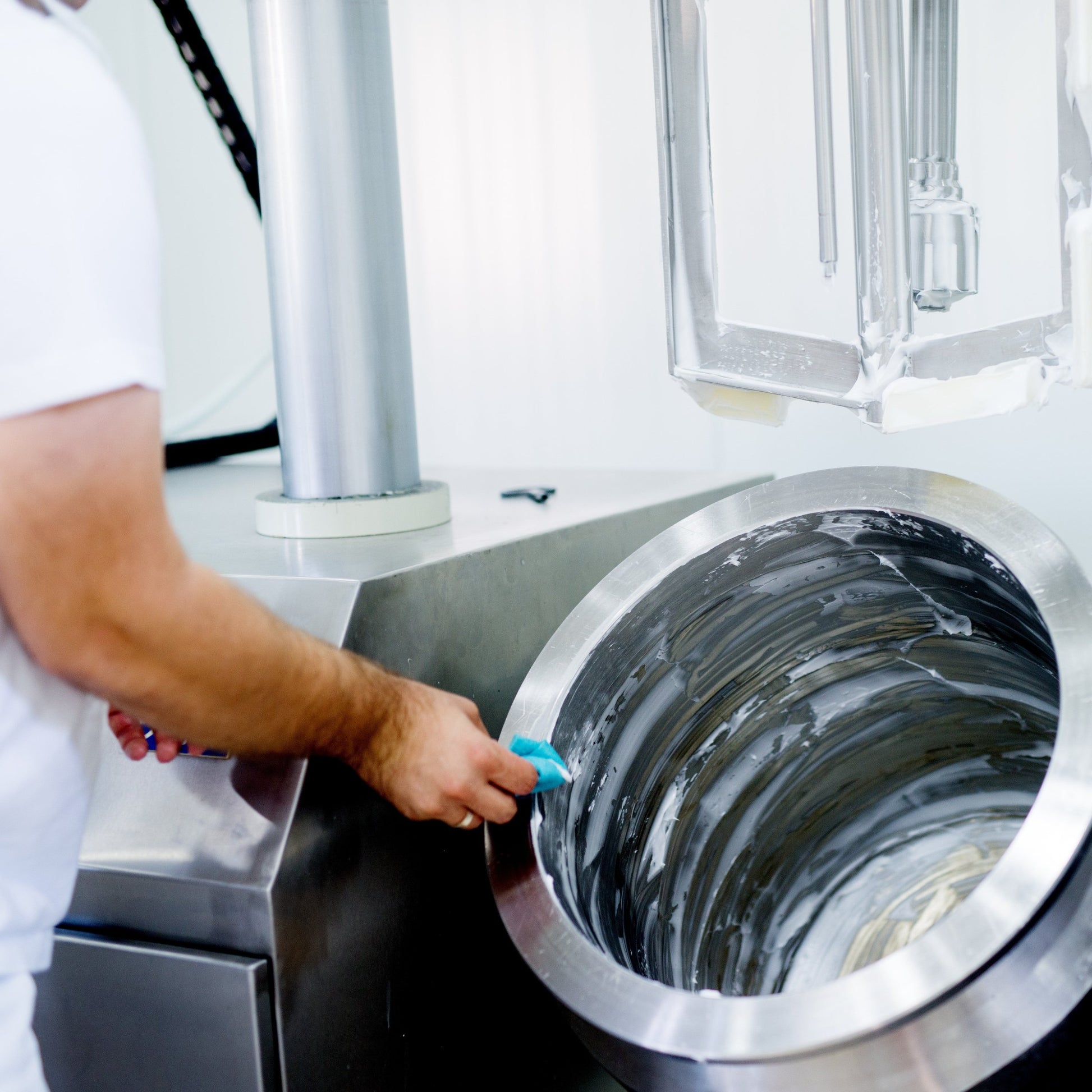 <Production operator wearing white cleaning a stainless steel mixing bowl, which has been used to manufacture liquid dietary supplements, in a white walled production area. Credit> AdobeStock_166858201