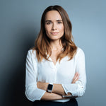 <Senior female quality manager wearing a white shirt, black skirt and e watch, stood against a grey wall with her arms folded for a corporate photograph. Credit> AdobeStock_170931593