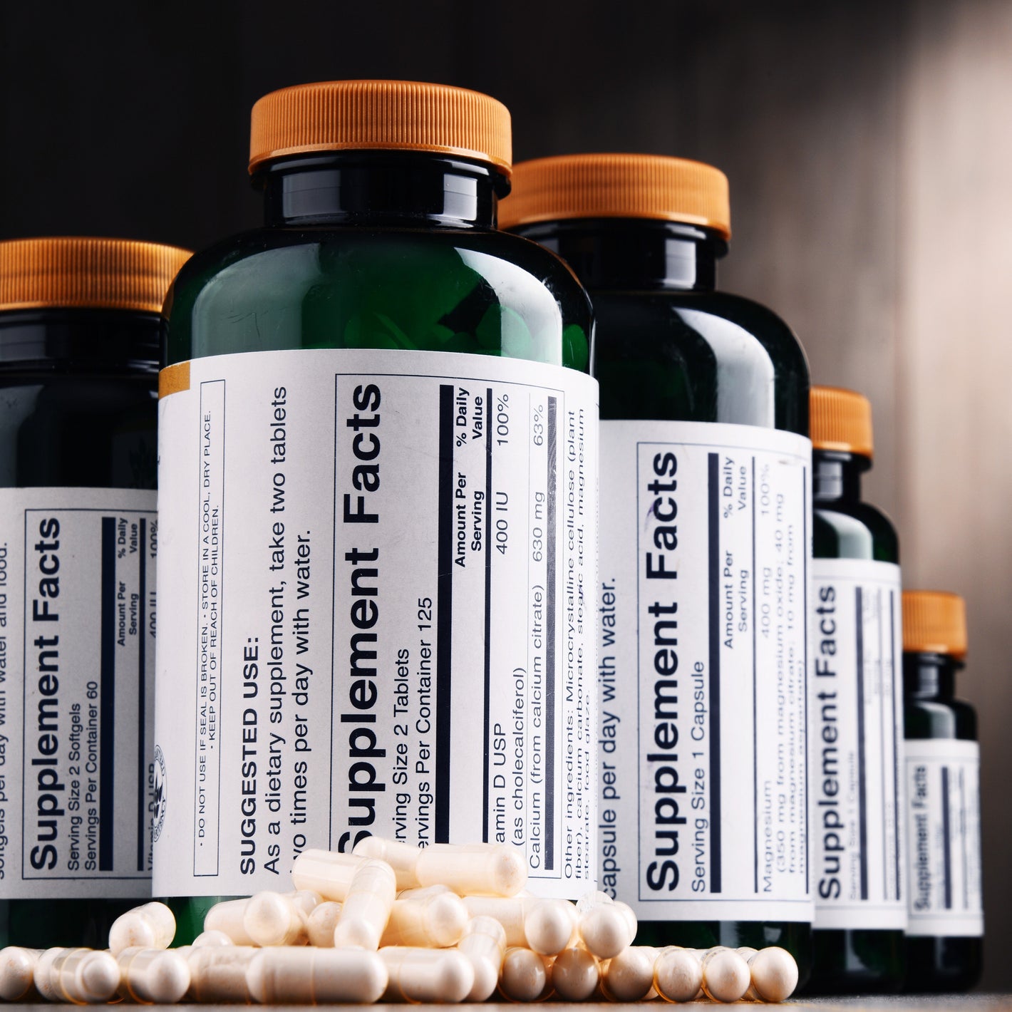 <White capsules on a table in front of amber brown plastic bottles with supplement facts labels, an example of which is one of the requirements of a batch production record for dietary supplements. Credit> AdobeStock_175842025