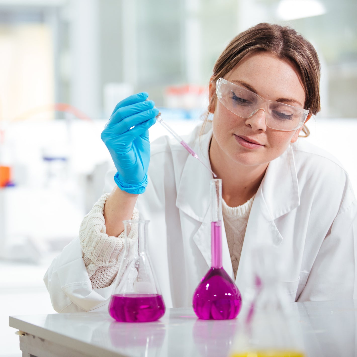 <Female lab analyst carefully pipetting a purple clear liquid into a glass volumetric flask. Credit> AdobeStock_198777510