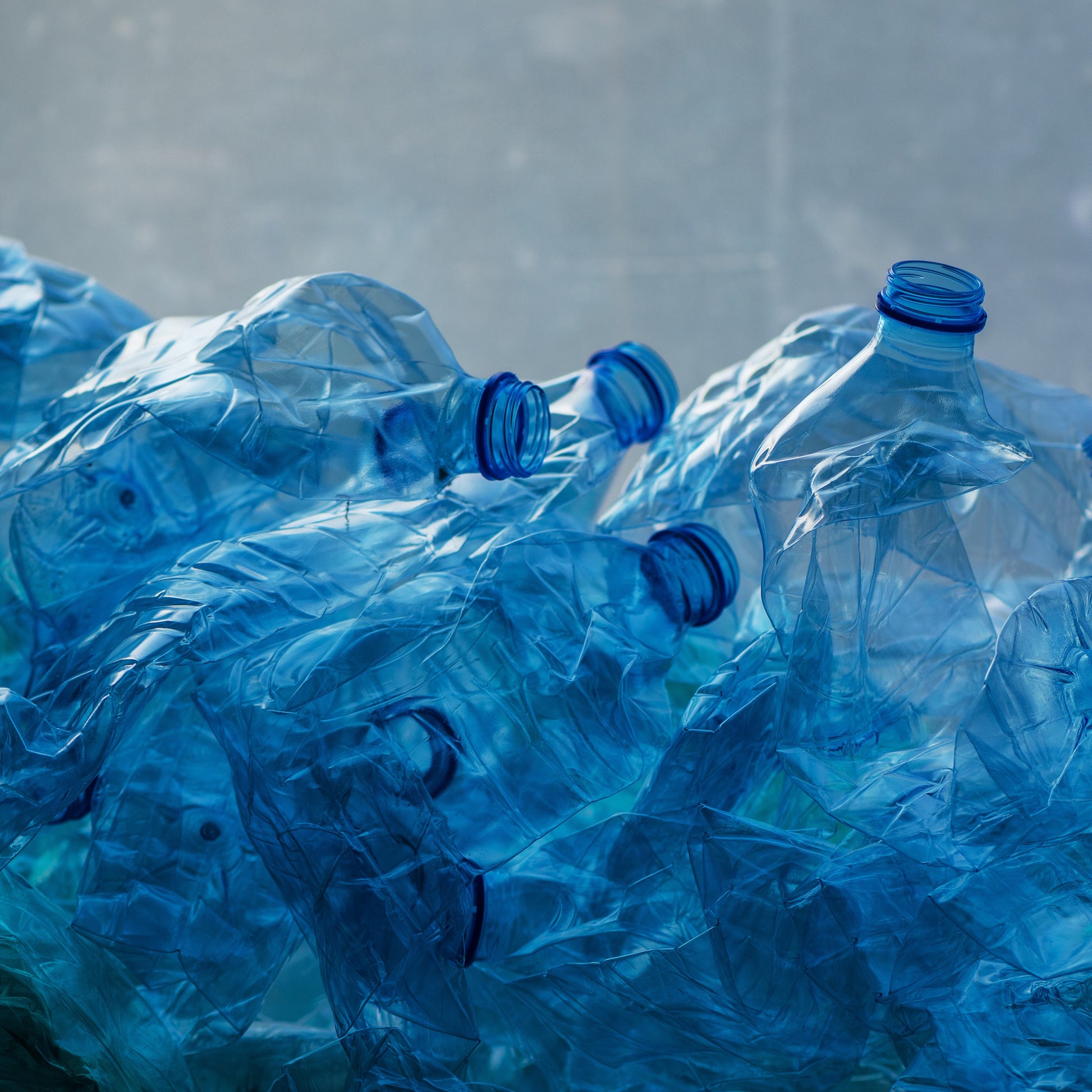 <Pile of damaged blue plastic bottles  lying on the concrete floor returned for recycling. Credit> AdobeStock_223169122