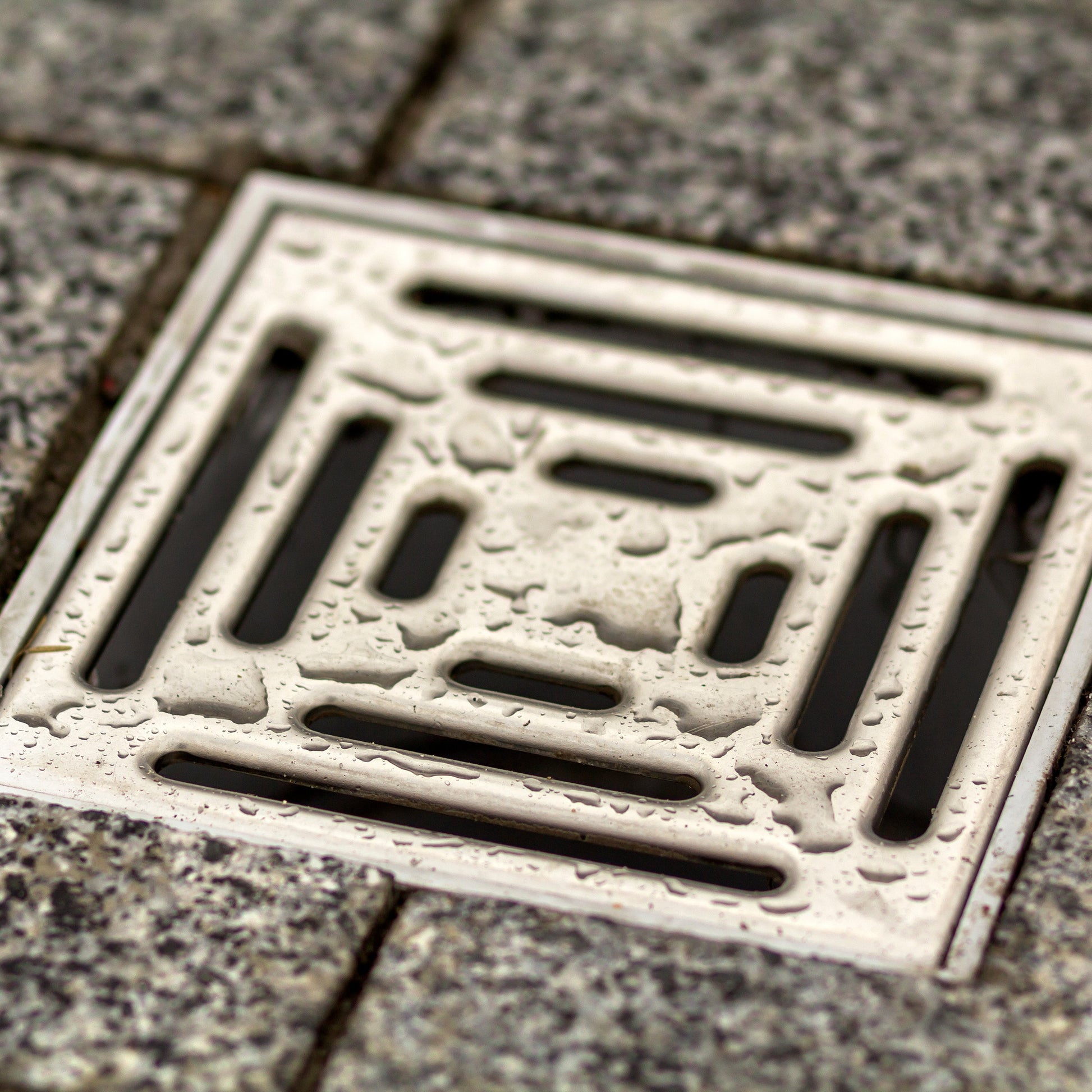 <Square, metal floor drain in a grey stone tiled floor. Credit> AdobeStock_245003730