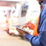 <Arms and body of man with fluorescent jacket and ipad checking in lorry deliveries to a dietary supplement warehouse. Credit> AdobeStock_251718231