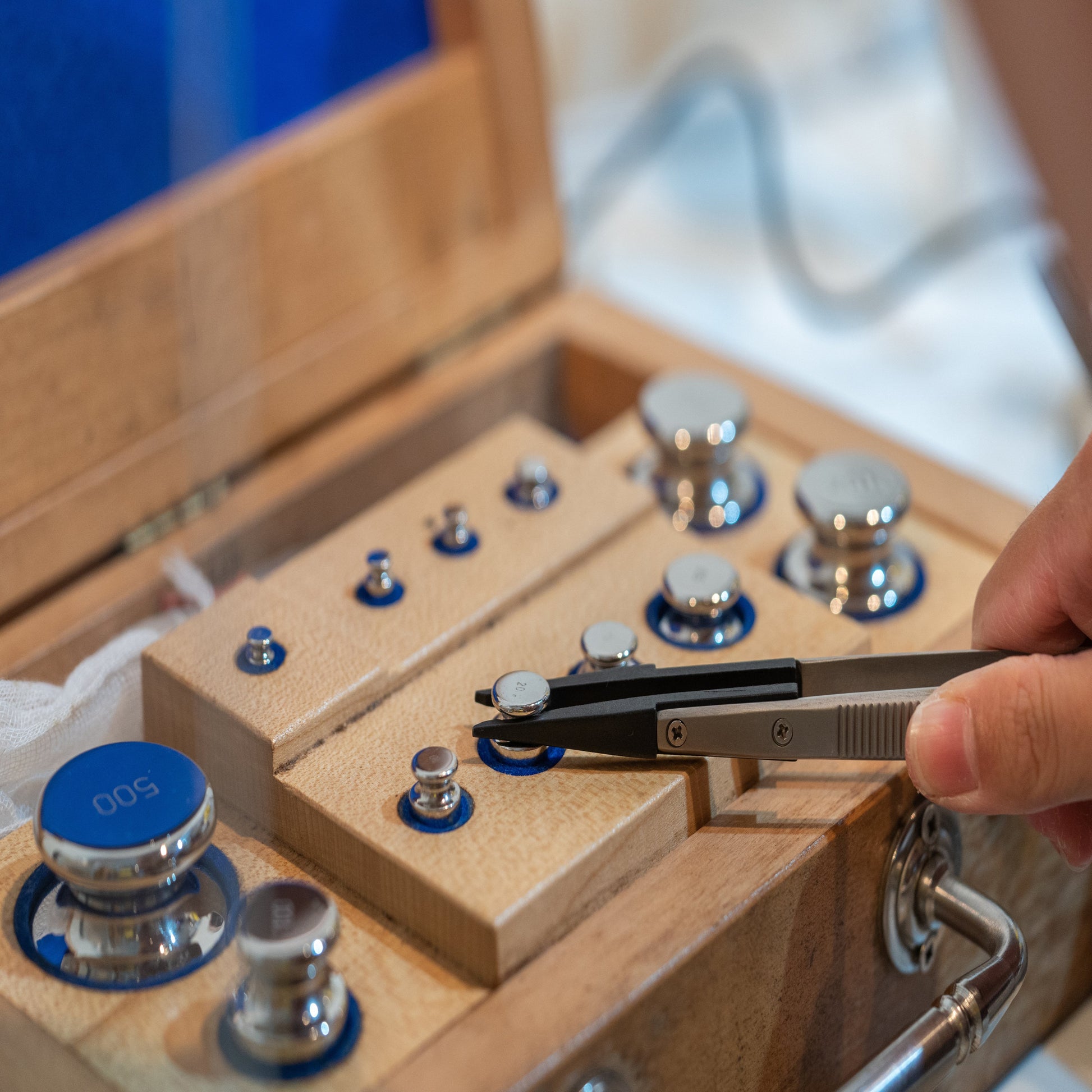 <Analyst taking a chrome calibration weight from a wooden box set with tweezers to calibrate an analytical balance. Credit> AdobeStock_274078427