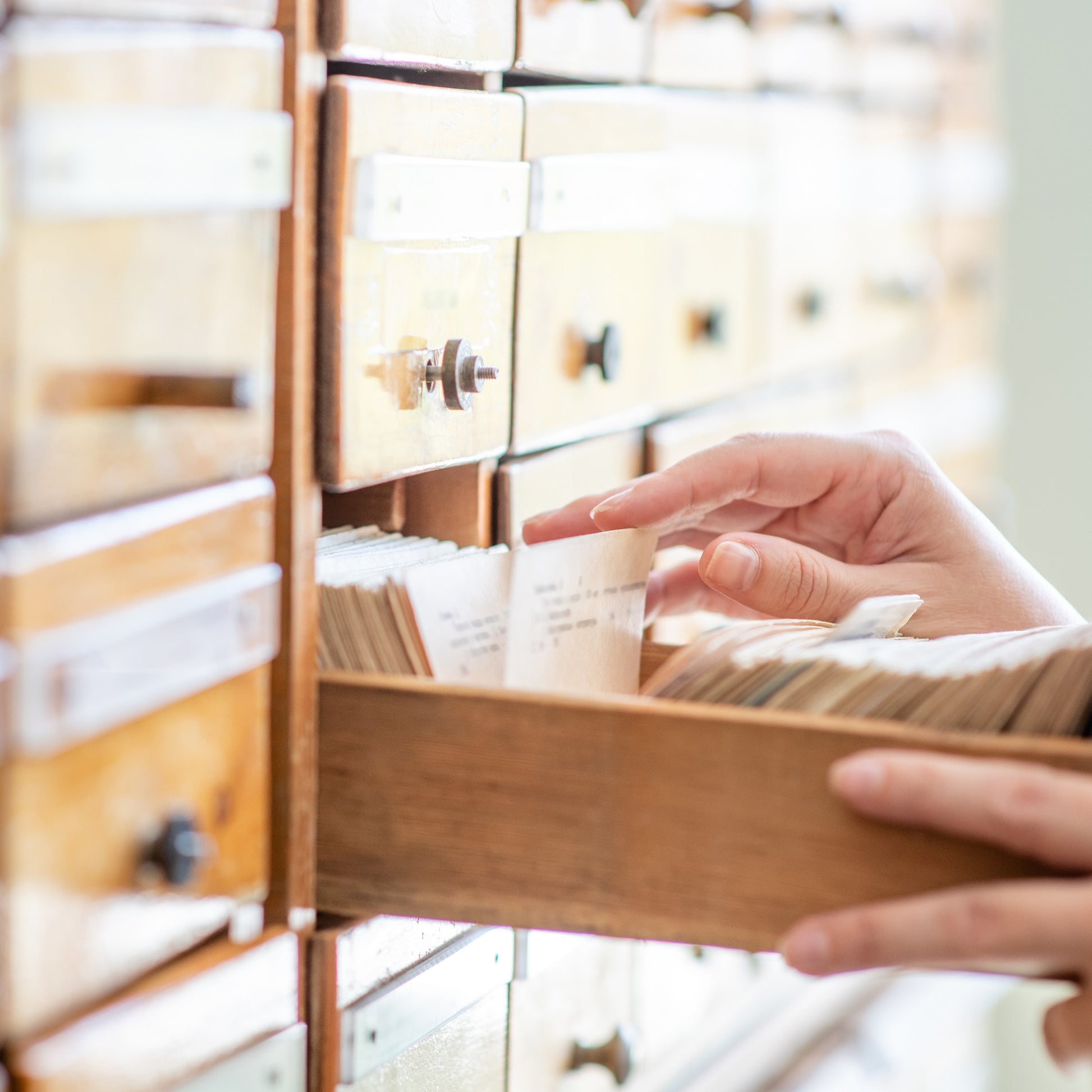 <Female hands searching through hand written records of old customer complaints kept on cards in a wooden box file drawer system. Credit> AdobeStock_284668162