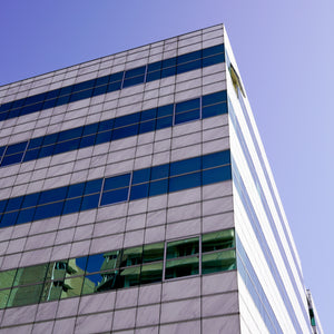 <Looking up at the corner of a grey, blue, and glass striped company office building or laboratories with sunny blue sky. Credit> AdobeStock_291035917