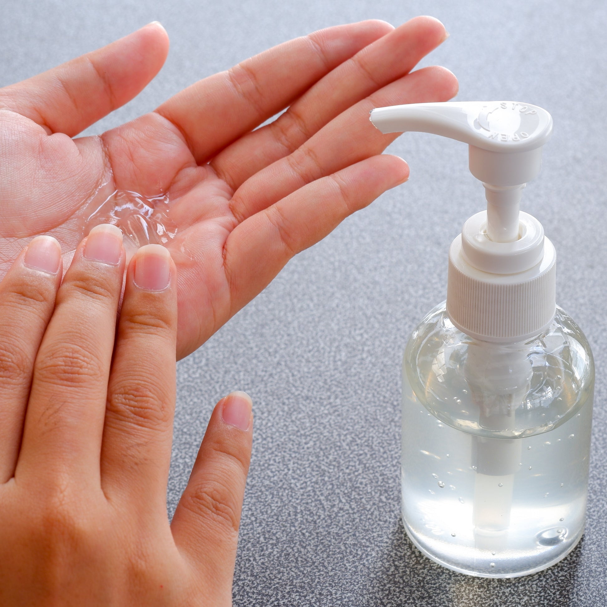 <Analyst checking a  sample of clear, anti-bacterial hand gel in a clear plastic bottle sat on a stone effect lab worktop with opaque white pump. The gel is of a viscosity that allows the correct amount to be pumped onto the hand and stays as a gel in the palm of the hand until rubbed. Credit> AdobeStock_328525929