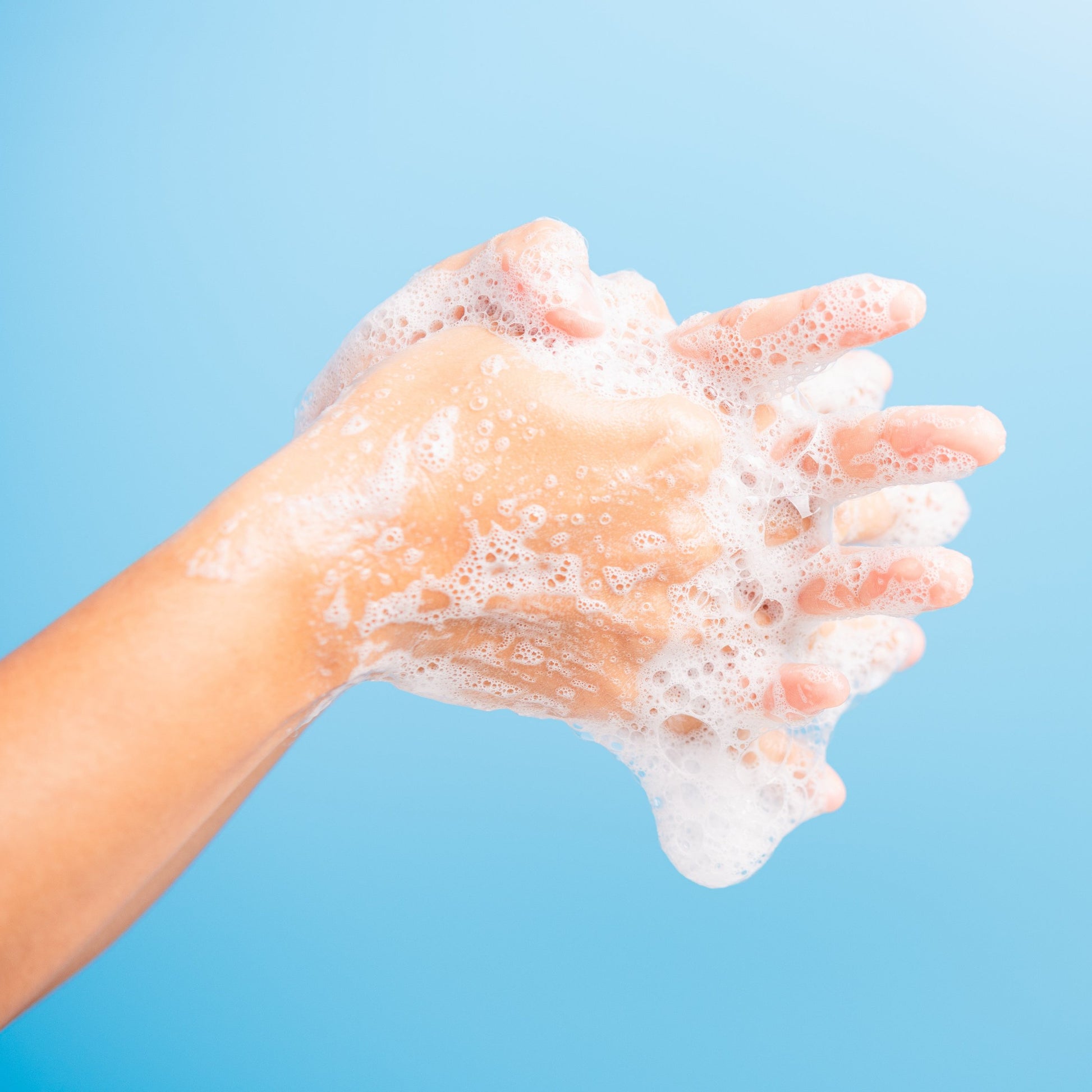 <Picture of two arms against a light blue background creating foam lather as they rub and wash their hands together,. Credit> AdobeStock_345027763