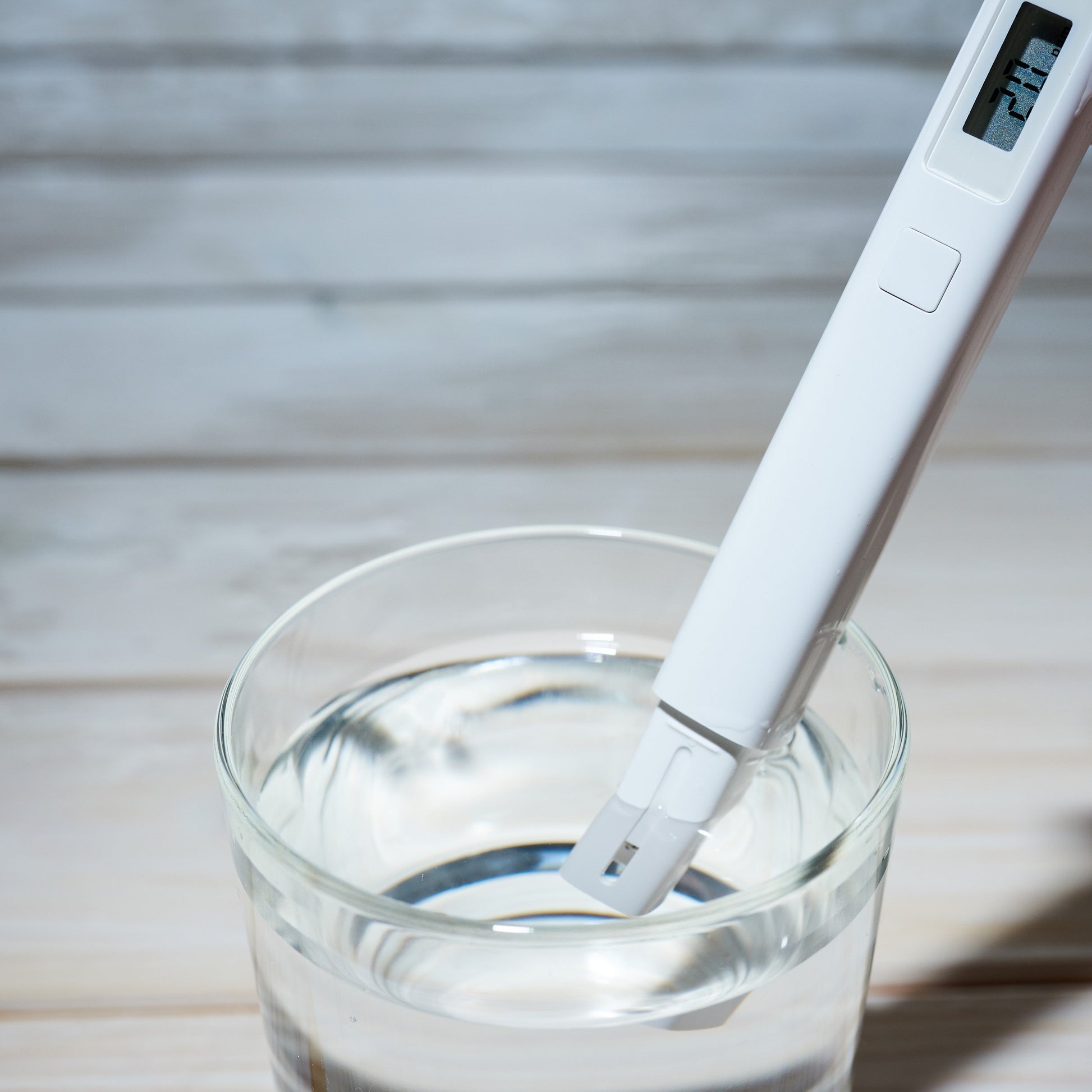 <Handheld digital conductivity meter as a white stick resting in a beaker of clear colourless liquid. Credit> AdobeStock_352578875