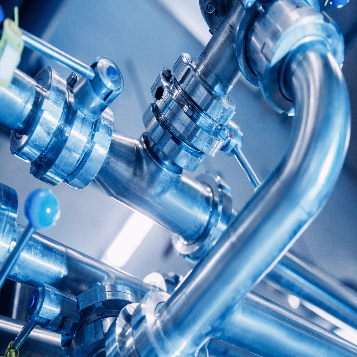 <Arrangement of stainless steel pipework, connectors and valves in a blue lit dietary supplement manufacturing facility transporting water and waste to the correct location. Credit> AdobeStock_388675579