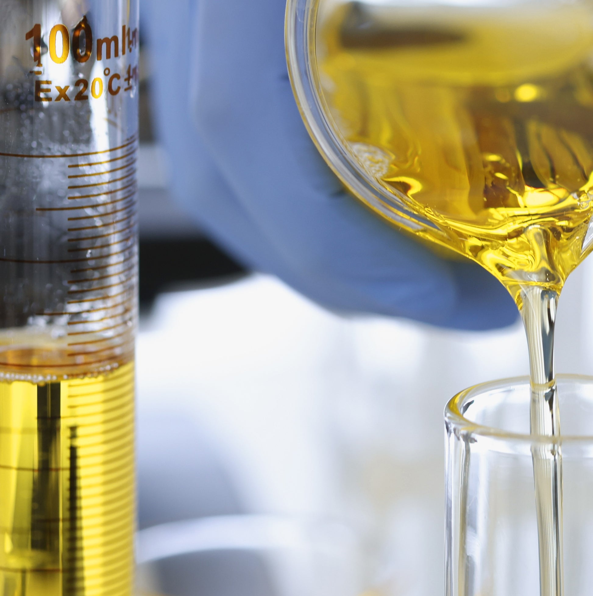 <Close up of analytical grade laboratory glassware being used to measure out a volume of amber, clear oily liquid. Credit> AdobeStock_395499068