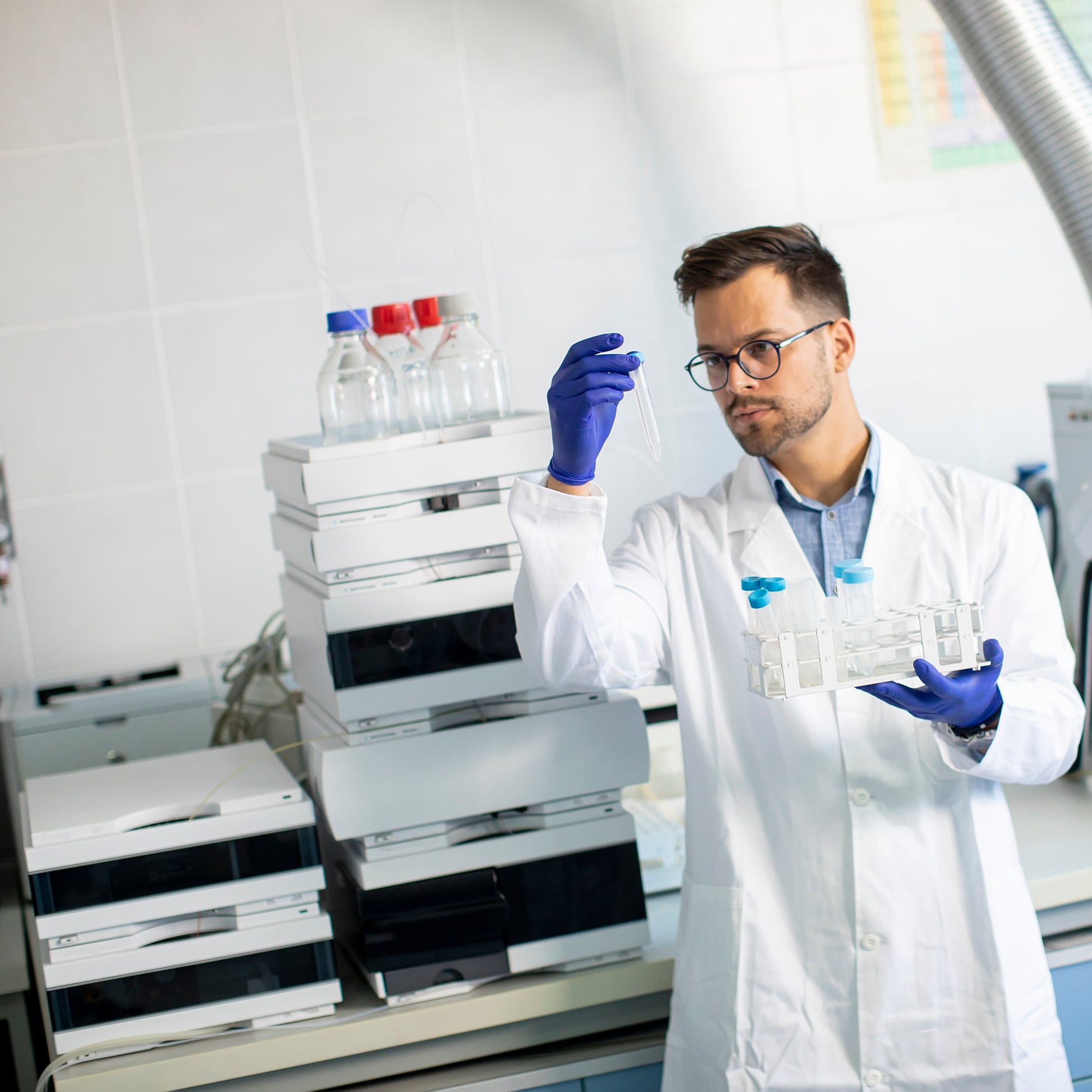 <Male analyst in labcoat and purple gloves in front of an HPLC preparing standards to run for dietary supplement assays. Credit> AdobeStock_403421068