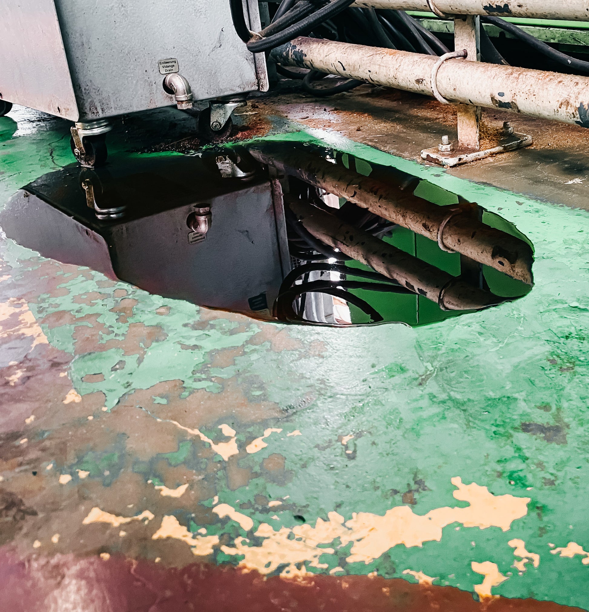 <Oil leaking from an old compressor onto a floor in a poor state of repair with paint peeling off and dirty. Credit> AdobeStock_403818552