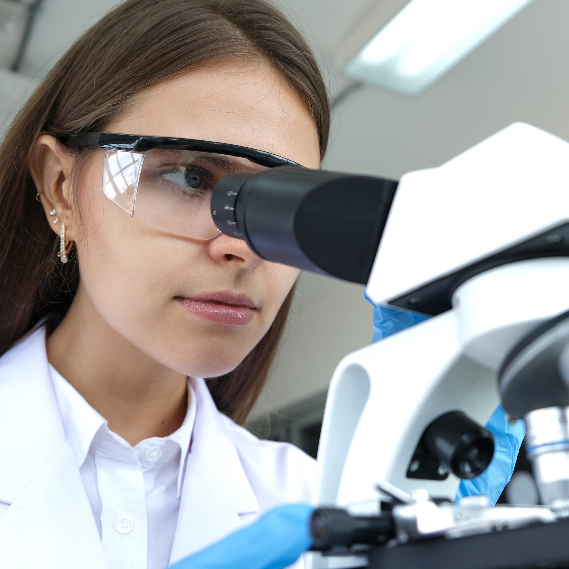 <Female laboratory analyst looking down the eyepiece of a black and white microscope. Credit> AdobeStock_427358393