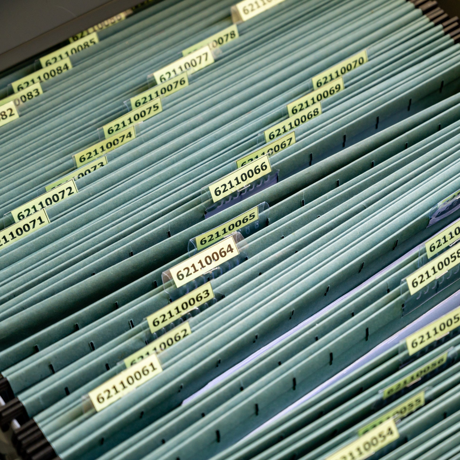 <Open cabinet drawer containing over 30 green cardboard hanging file folders individually numbered and in numerical order with 8 digits starting in 6211. Credit> AdobeStock_451517968