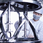 <Male operator stood next to the raised lid of a polished stainless steel mixing tank with attached agitator stirrers. Credit> AdobeStock_456575470