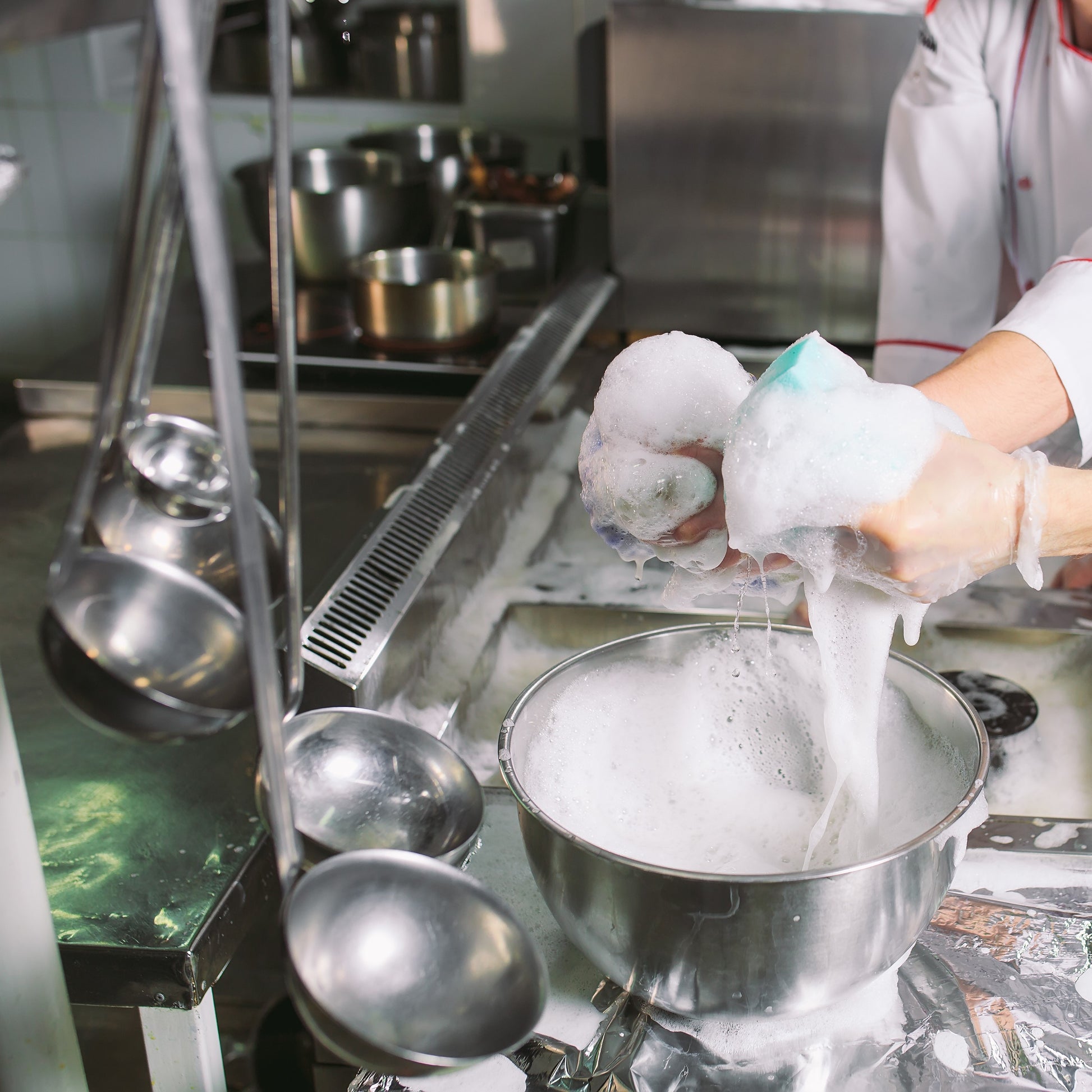 <Stainless steel mixing bowls and utensils used to manufacture dietary supplements being cleaned in a steel sink with foaming hot water. Credit> AdobeStock_458221990