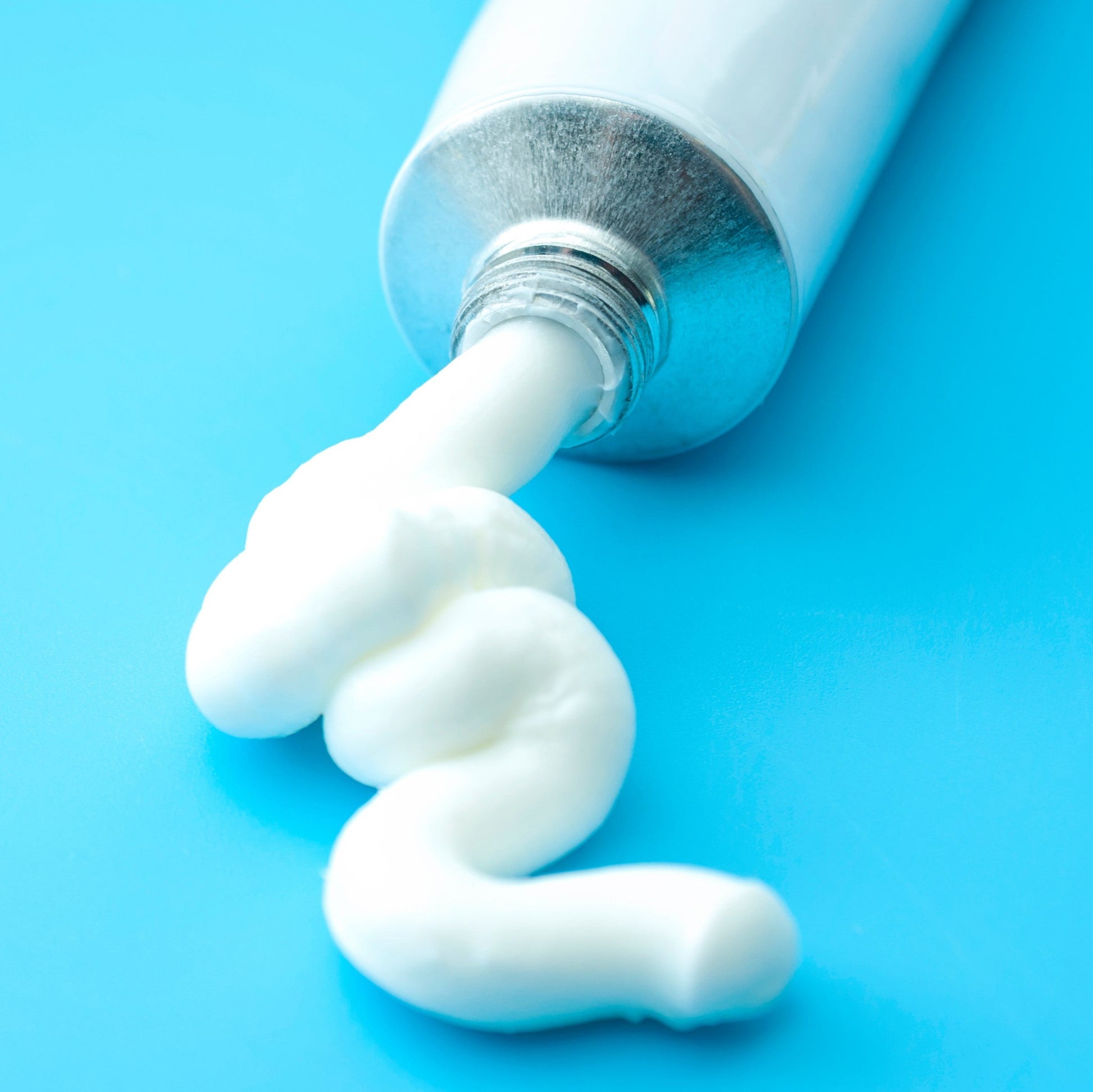 <Viscous but maybe aerated cream dispensed from a white aluminium tube onto a bright light blue surface and holding its shape. Credit> AdobeStock_462525889