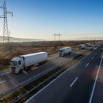 <Convoy of white lorries distributing supplements on a dual carriageway, blue sky, morning sunlight, hills, scrubland and electricity pylons in the background. Credit> AdobeStock_464144081