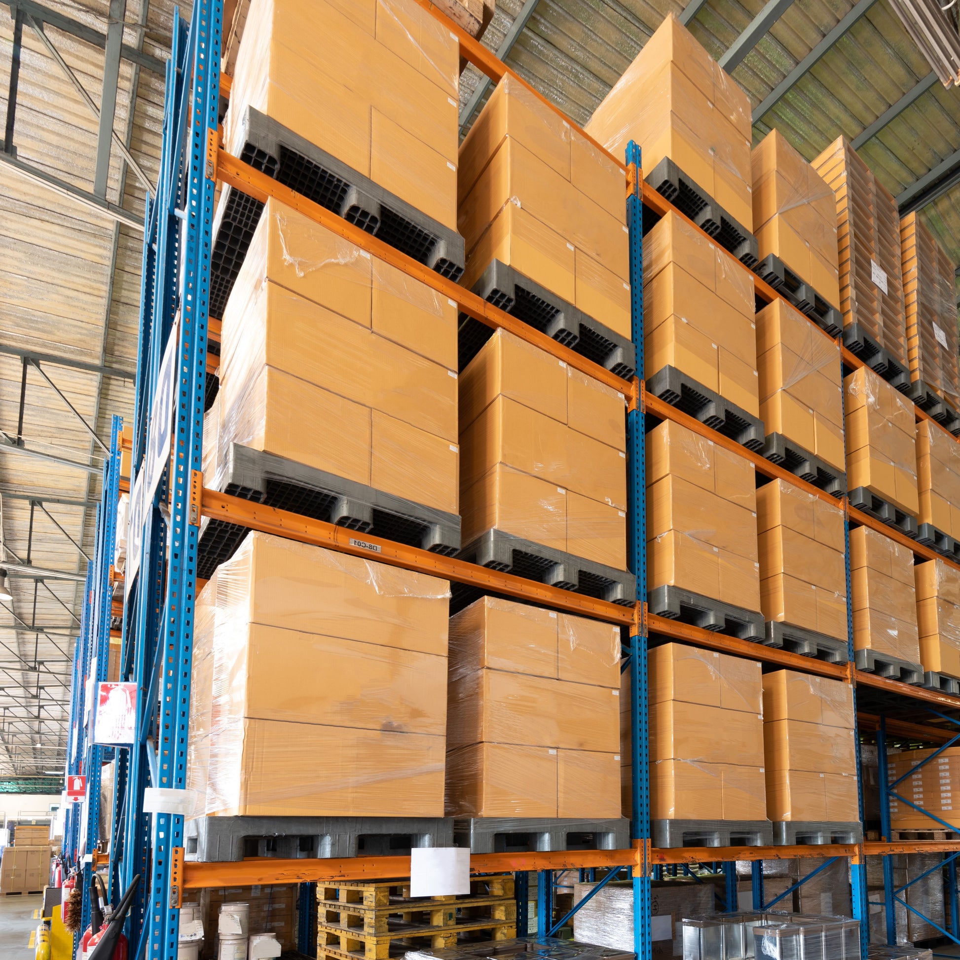 <Rows of cardboard boxes of packaging materials on wooden pallets on orange and blue warehouse racking. Credit> AdobeStock_477083814