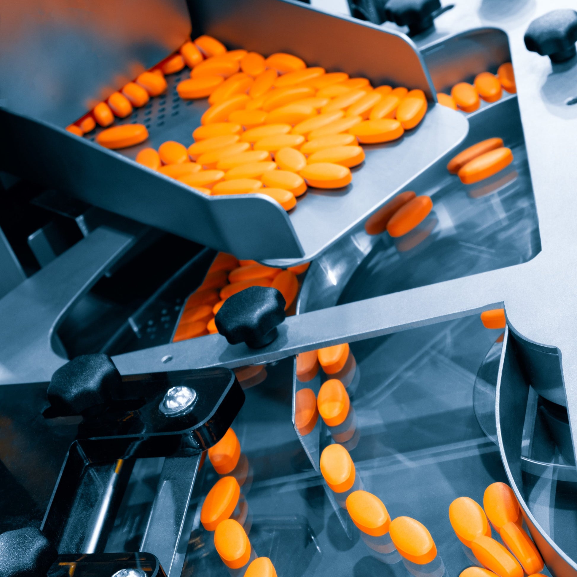 <Yellow dietary supplement tablets moving down a metal chute onto a rotary tablet filling machine to be aligned ready for packing. Credit> AdobeStock_477674087