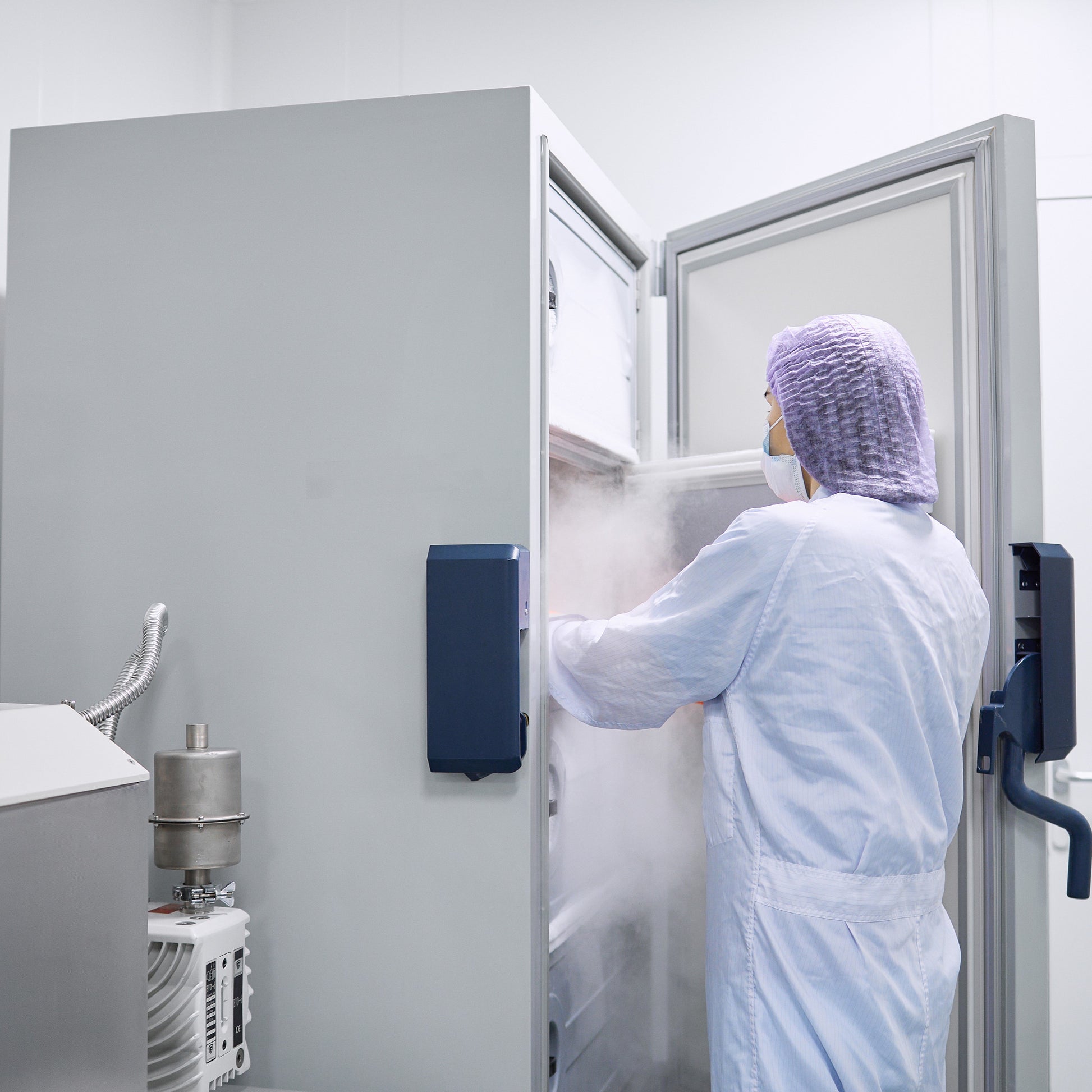 <Stability analyst wearing lab coat and hairnet removing samples for testing from a single door temperature and humidity controlled stability chamber. Credit> AdobeStock_500284461