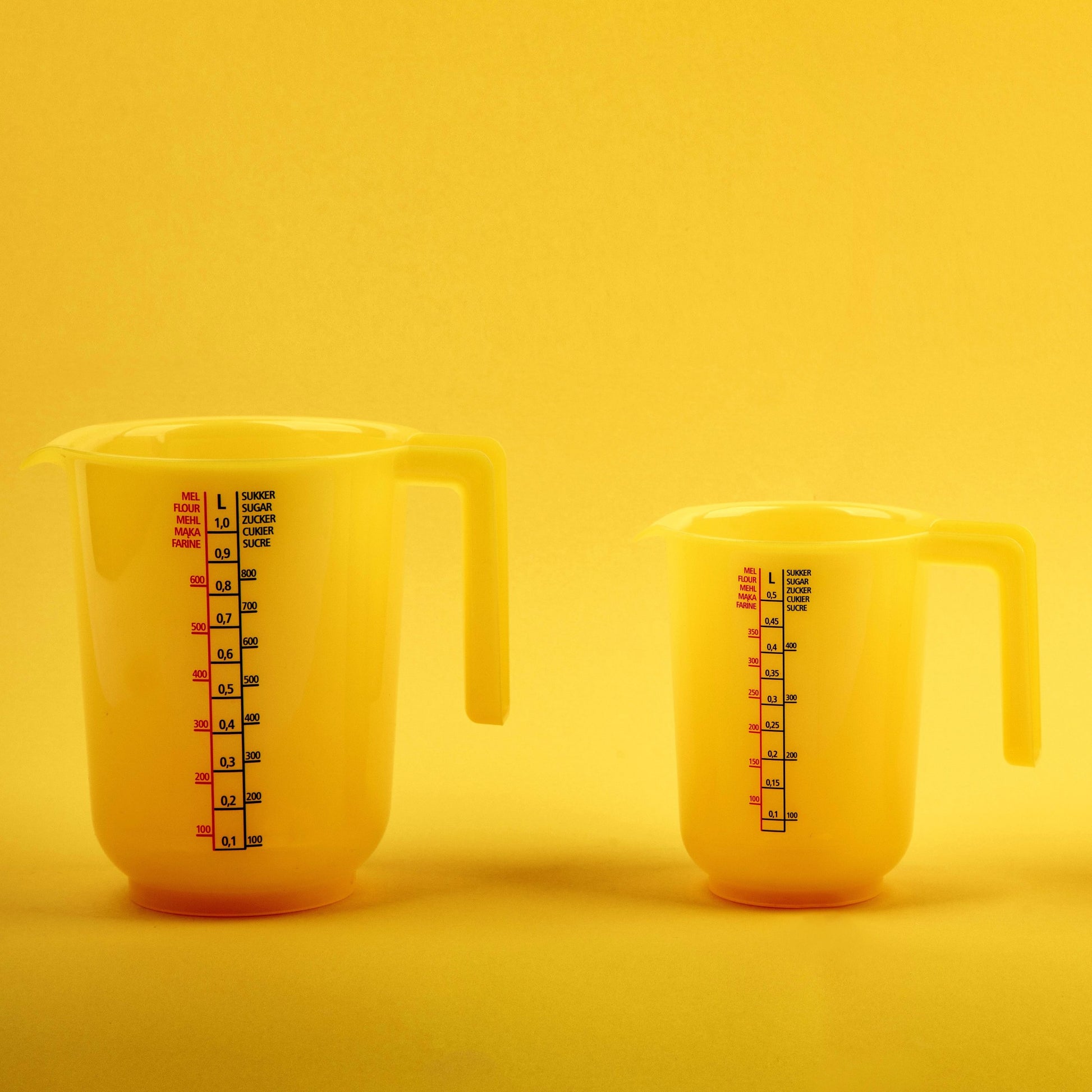 <One large and one medium plastic jug, used for measuring the volume of liquid supplement ingredients, sitting on a smooth surface with a bright yellow lit background. Credit> AdobeStock_544731939