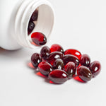 <Dark burgundy red, clear gel capsules of anti-oxidants being poured out of a white plastic bottle onto a white surface. Credit> AdobeStock_731519422