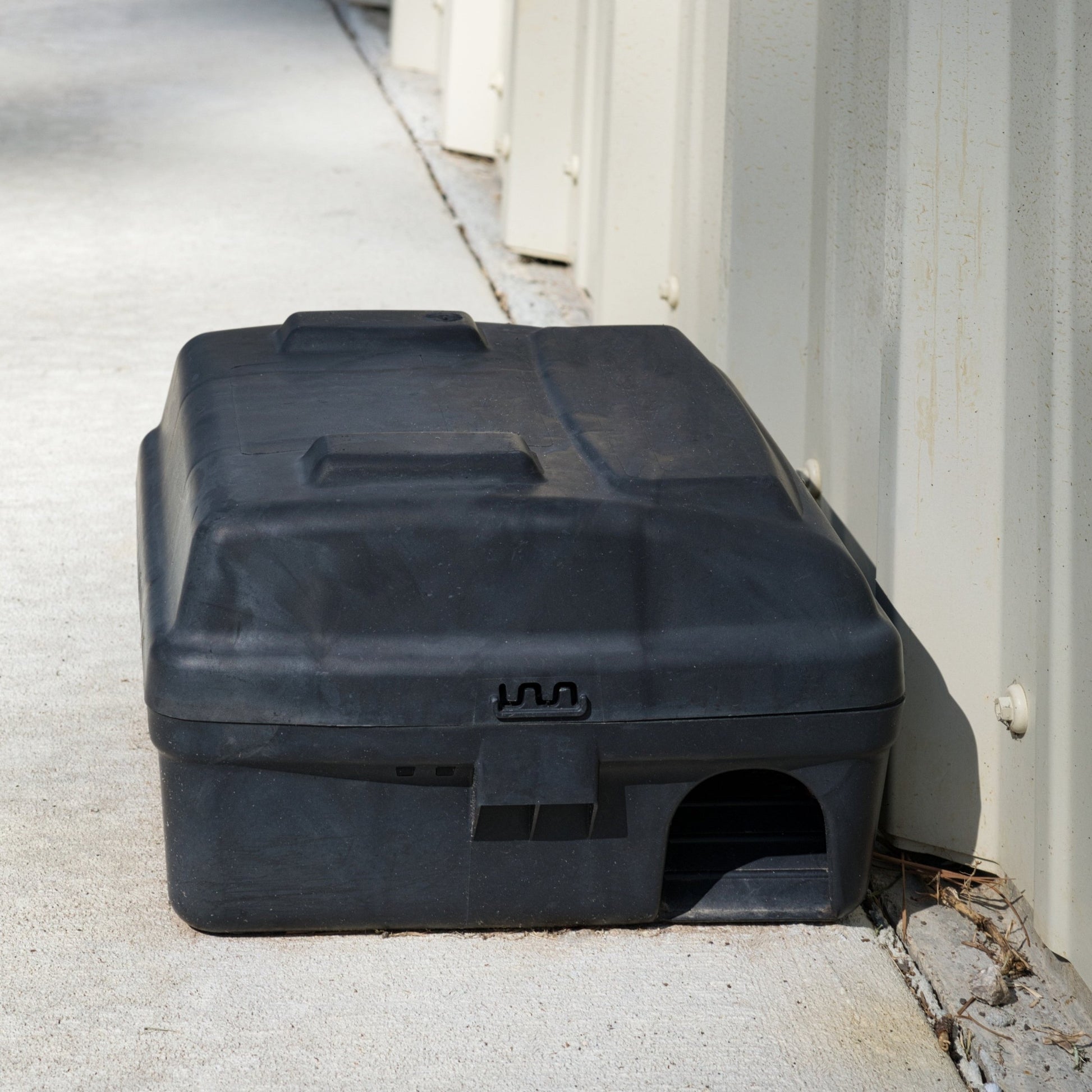 <Black rodent rat or mouse bait station trap box placed along the corrugated metal wall of a warehouse by a pest control specialist. Credit> AdobeStock_735478741