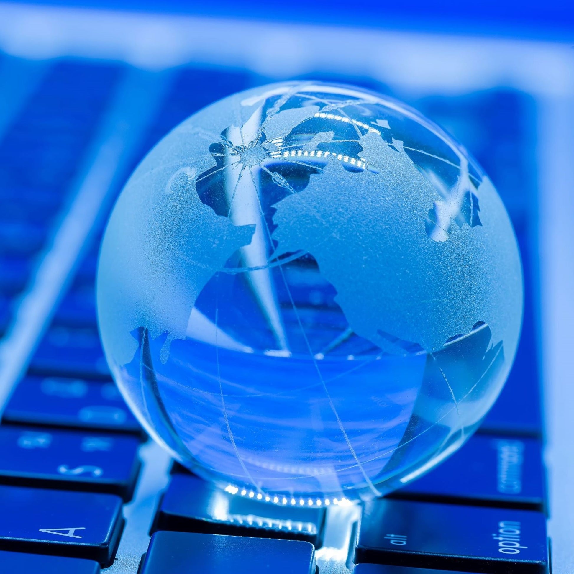 <Clear and etched glass globe of the world sat on the blue keyboard of a laptop representing how global trade can be conducted online. Credit> jcomp @ Freepik