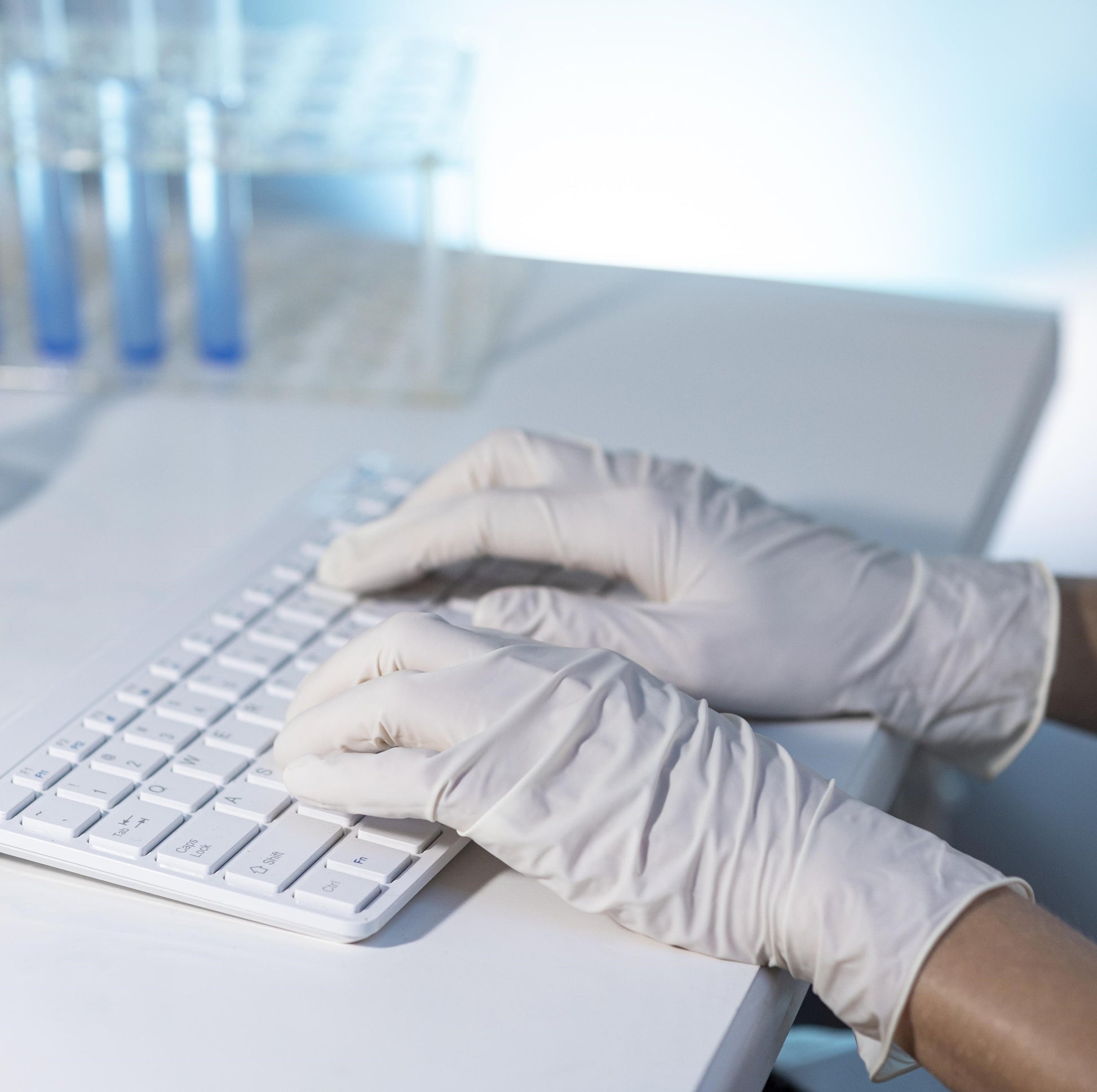 <Laboratory analyst entering data electronically by white keyboard on the laboratory information management system LIMS next to a test tube rack with three blue tubes. Credit> Freepik