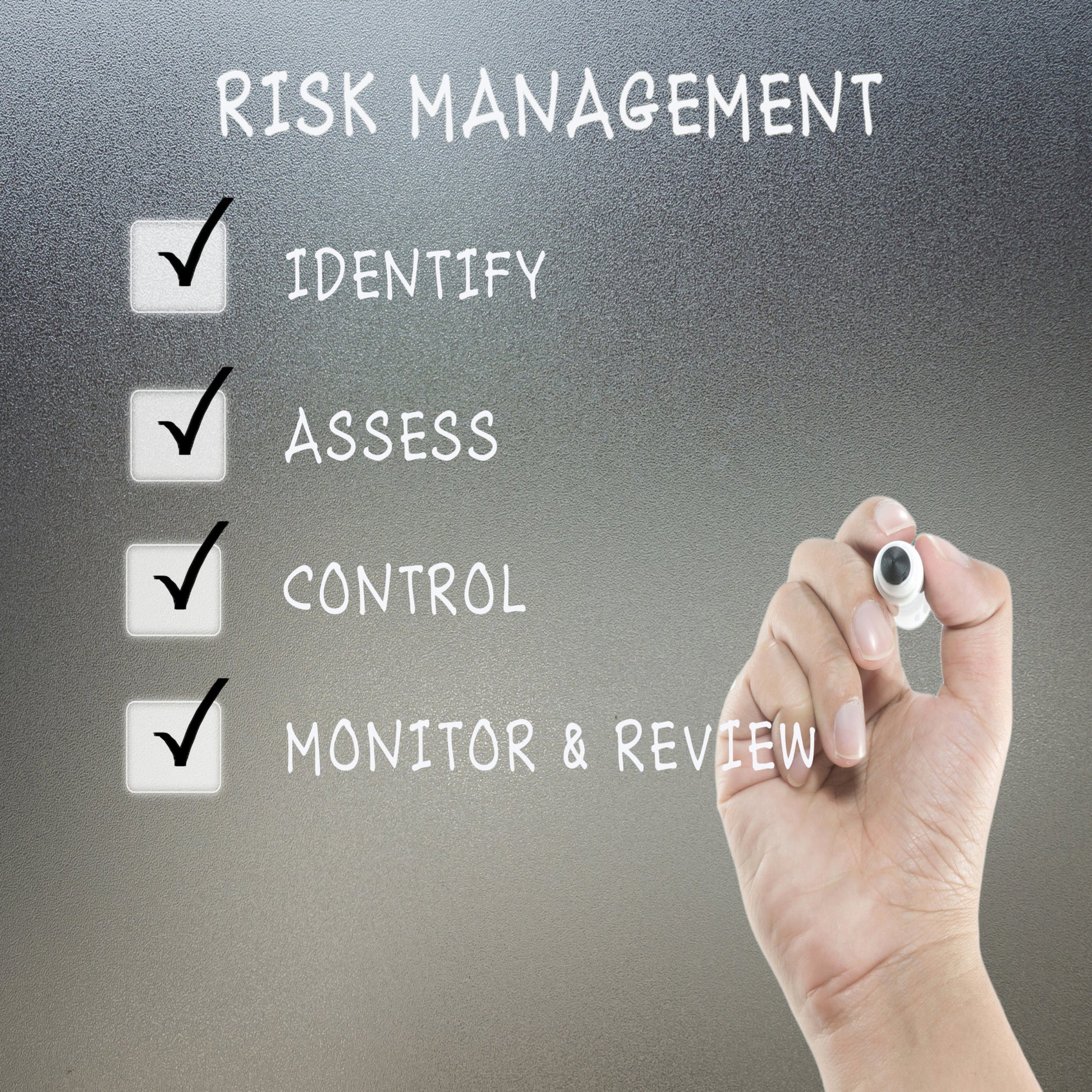 <Hand with marker pen writing on frosted safety glass the four stages of Risk Management, identify, assess, control, and monitor or review with a tick in a box against each. Credit> 52721976 © Tameek | Dreamstime.com