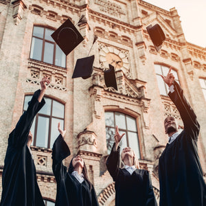 <Four university college graduates, two male and two female, stood outside the university wearing graduation gowns throwing their mortarboard hats in the air in celebration of qualifying. Credit> 98006981 © Vasyl Dolmatov | Dreamstime.com