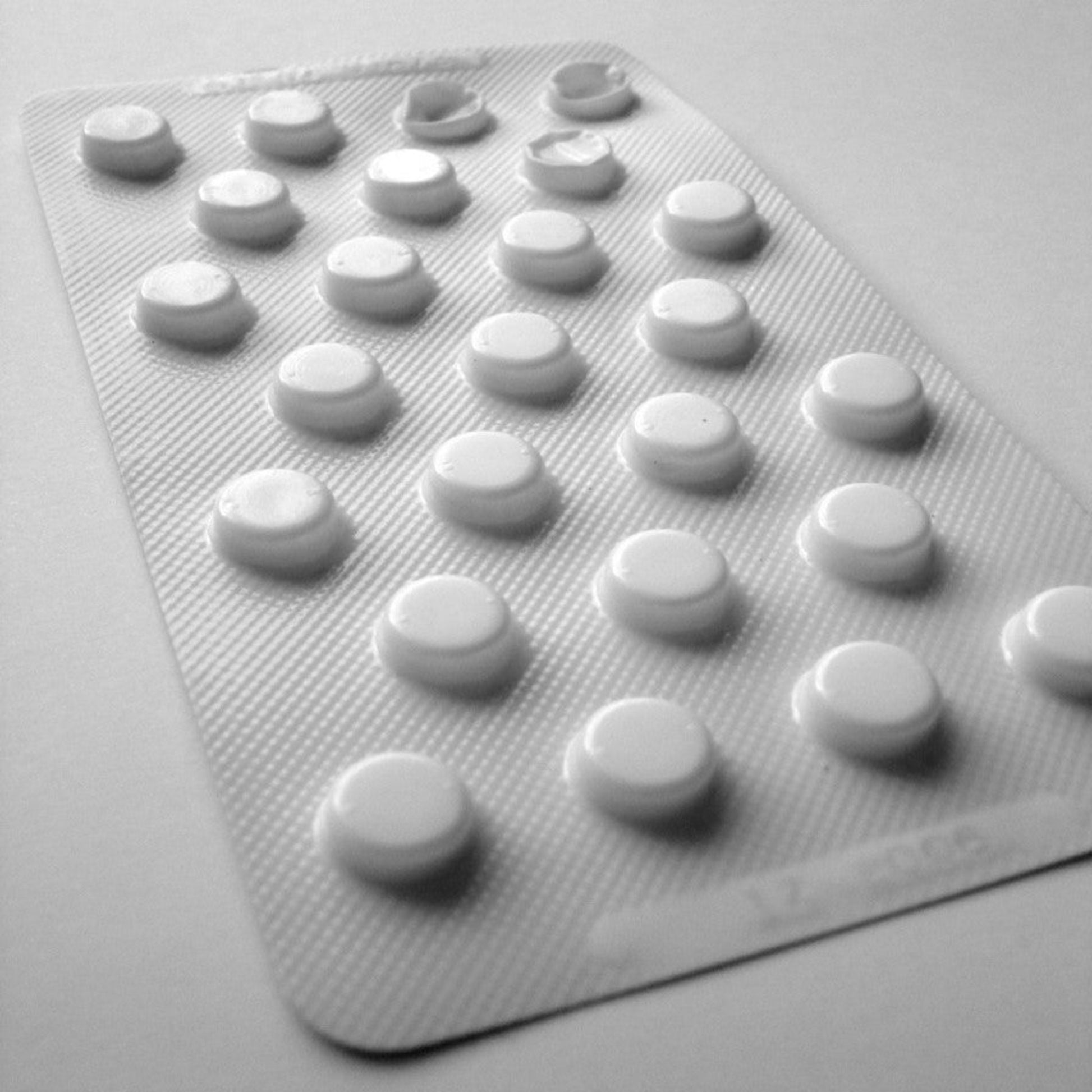 <Close up of a white plastic foil blister sheet containing 25 tablets where 3 from the top right hand corner have been pressed out and used, sitting on a white surface. Credit> 1328288 by secureroot @ freeimages