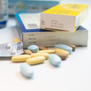 <Expiration dates from stability studies on two cartons of different medicine products on a white table with some yellow, brown and blue oval tablets in front of them. Credit> 2141323401 © Kasarp Studio | Shutterstock.com