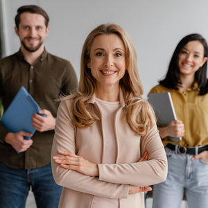 <Three smiling employees, a female with her arms folded standing in front of a man and a woman holding notepads. Credit> Freepik 