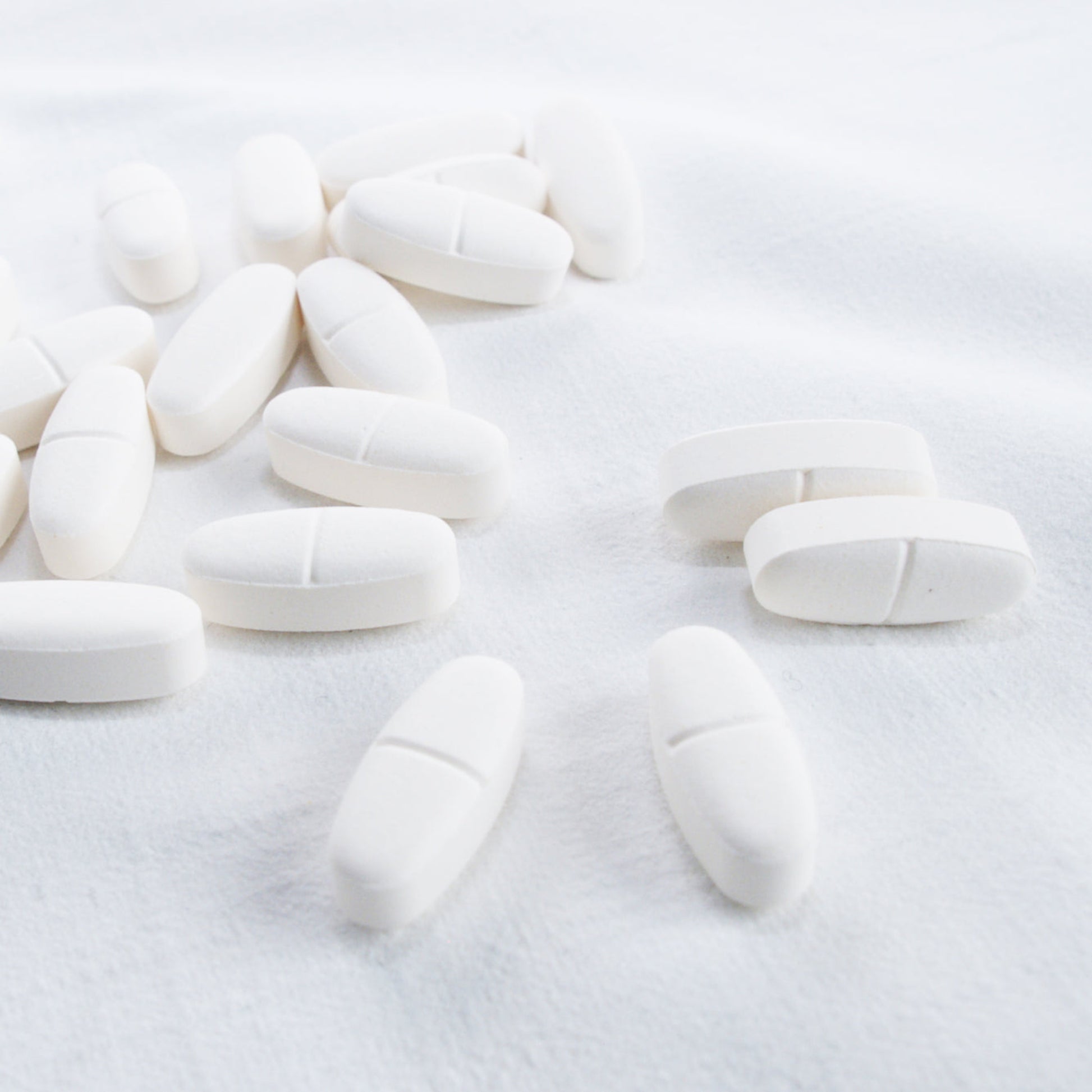 <Oval white tablets with centre break line on a white linen cloth. Credit> 1173911 by leagun @ freeimages